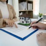 Una agente inmobiliaria señala con un dedo la parte de un contrato donde tiene que firmar el hombre con el bolígrafo en la mano