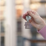 Una mano coge unas llaves con una llavero de madera de una casa. Simbolo de nueva casa o primera vivienda.